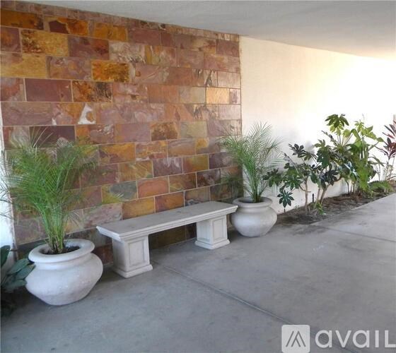 A bench sits in front of a brick wall with potted plants on either side.