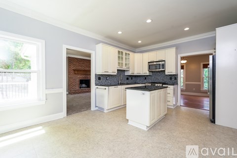 A kitchen with white cabinets and a black backsplash is available for rent.