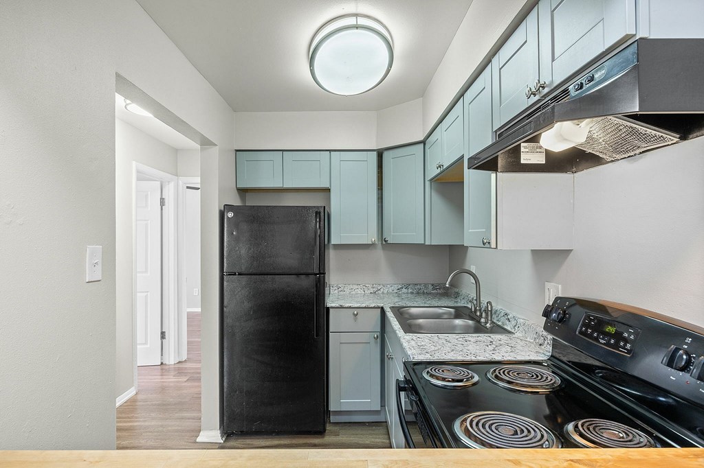 A kitchen with a black fridge and stove top oven.