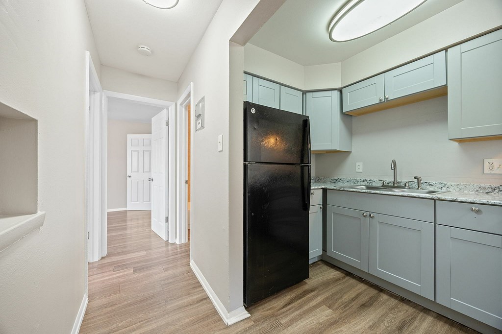 A black refrigerator in a kitchen with wooden floors and white walls.