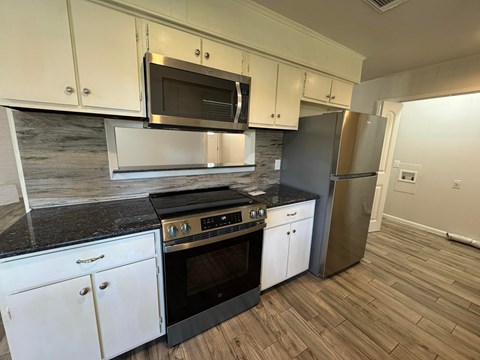 A kitchen with white cabinets and black countertops.