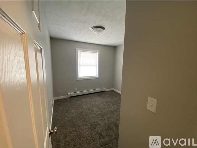 A room with a carpeted floor, a window, and a door.