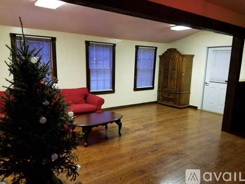 A Christmas tree stands in a living room with a red couch and a wooden cabinet.