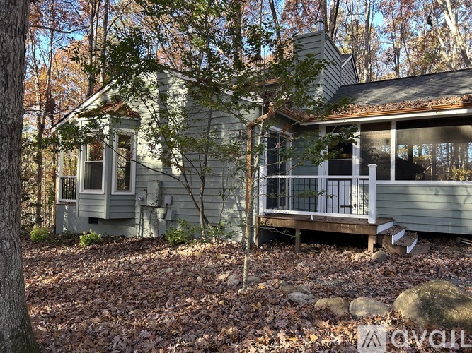 A small house with a porch is surrounded by trees.