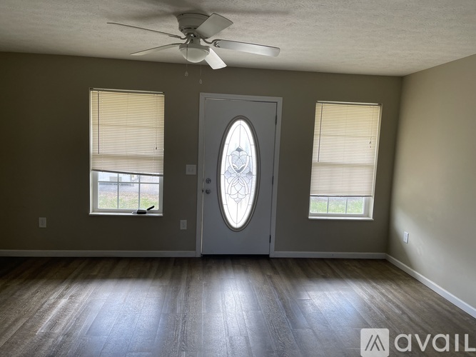 A room with a ceiling fan, two windows with blinds, and a door with a glass window.