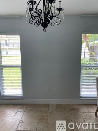 A room with a chandelier, two windows with blinds, and a chair.