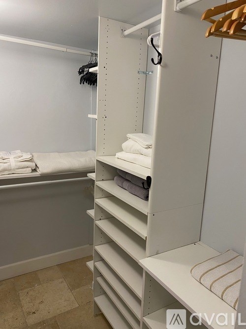 A white closet with a towel on a shelf and a bathtub in the background.