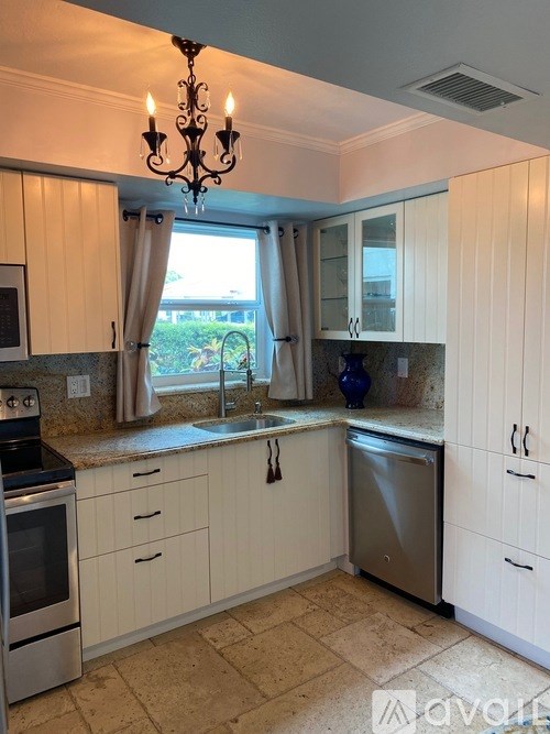 A kitchen with a chandelier, stove, sink, and cabinets.