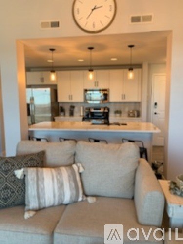 A living room with a grey couch and a clock on the wall.