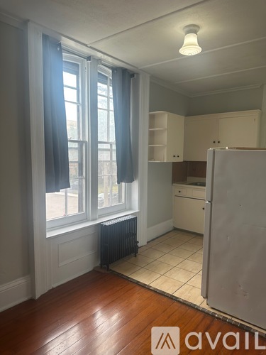A kitchen with a refrigerator, cabinets, and a window with curtains.
