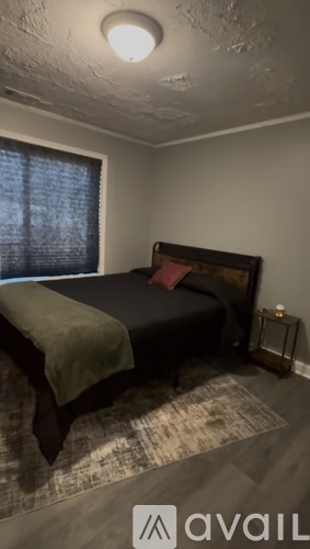 A bedroom with a bed, a window with blinds, and a rug on the floor.