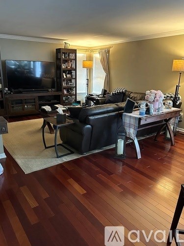 A living room with a black leather couch and a wooden floor.