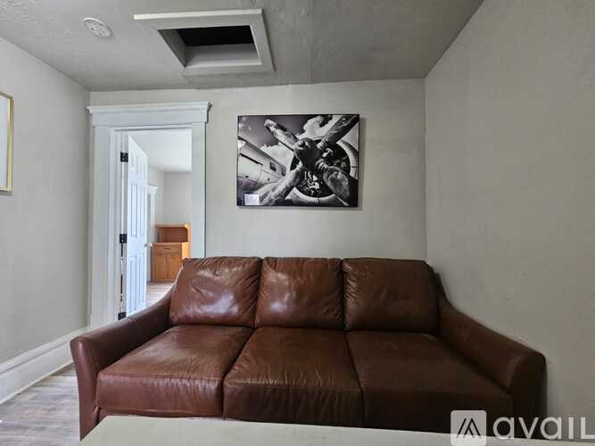 A brown leather couch is in the foreground of a room with a painting on the wall.