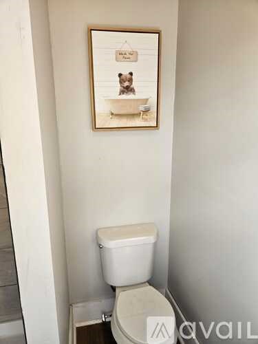 A white toilet in a bathroom with a framed picture of a cat on the wall.