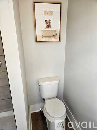 A white toilet in a small bathroom with a picture of a woman in a bathtub hanging on the wall.