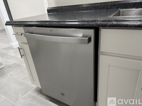 A kitchen with a black counter top and a stainless steel dishwasher.
