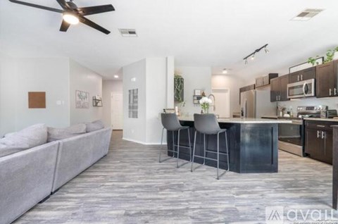 A modern living room with a grey sofa and a kitchen area with brown cabinets.