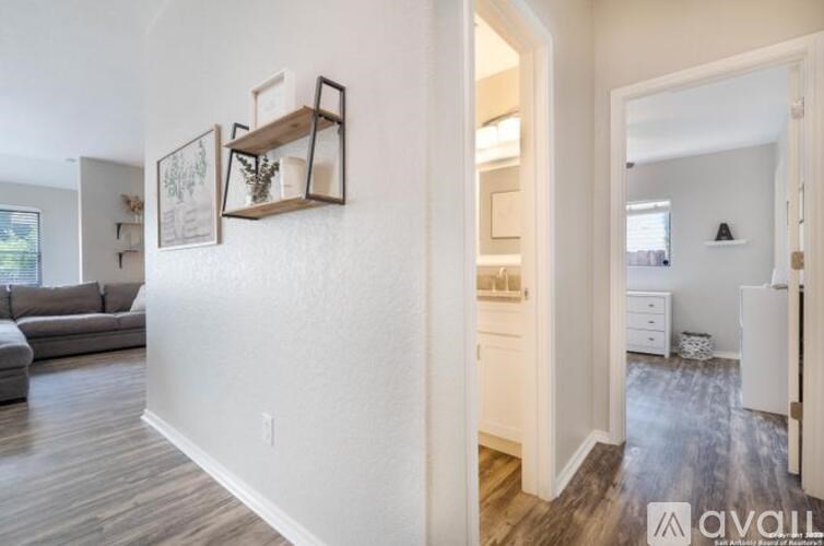 A living room with a grey couch and a white wall with a shelf and picture frames.