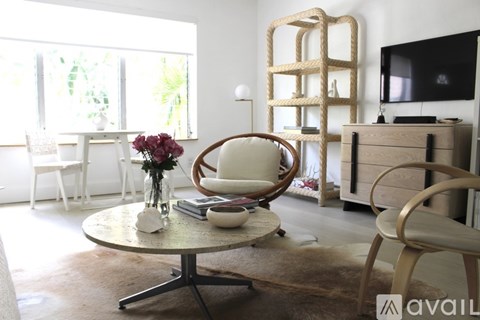 A living room with a white chair and a round table with a vase of flowers on it.