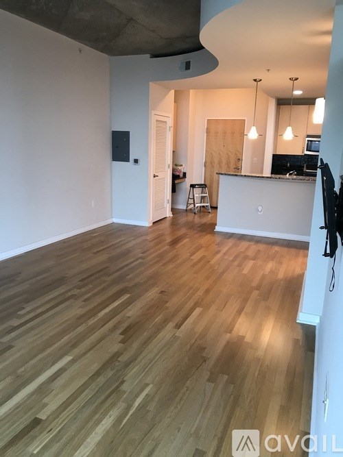 A room with wooden flooring and a kitchen area in the background.