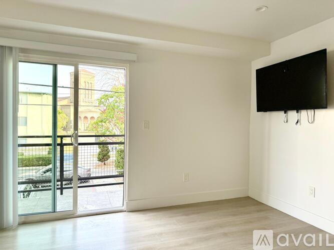 A spacious room with a flat screen TV mounted on the wall and sliding glass doors leading to a balcony.