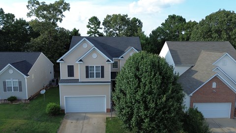 A house with a garage is surrounded by other houses and trees.