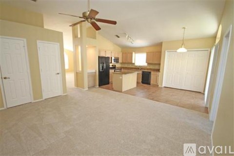 A living room with a fan and a kitchen in the background.