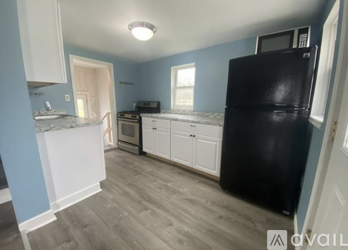 A kitchen with a black fridge, white cabinets, and a marble countertop.
