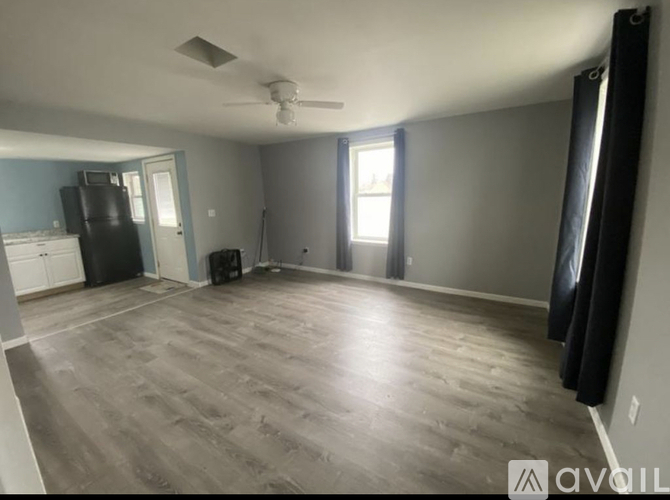 A spacious room with a ceiling fan and light, a black sofa, and a wooden floor.