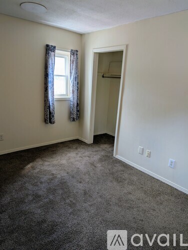 A room with a carpeted floor, a window with curtains, and a door leading to another room.