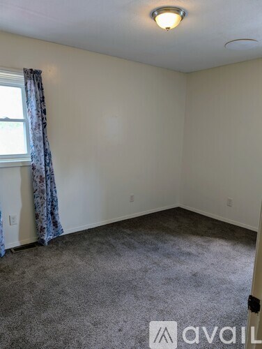 A room with a carpeted floor and a window with curtains.
