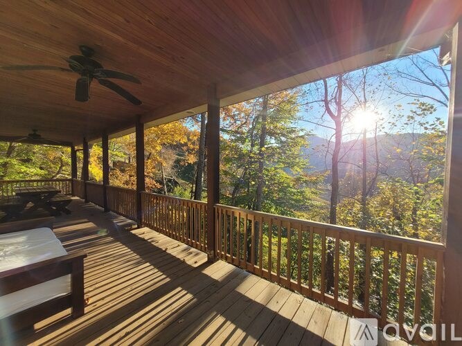 A wooden deck with a ceiling fan and a view of the forest.
