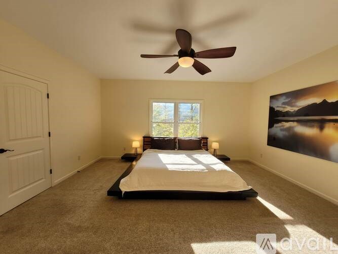 A bedroom with a bed, a ceiling fan, and a painting on the wall.
