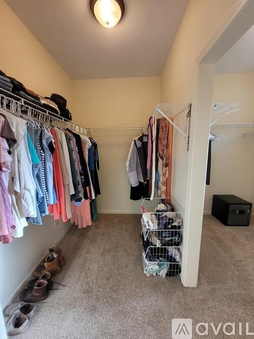 A small closet with clothes hanging on a rail and shoes on the floor.