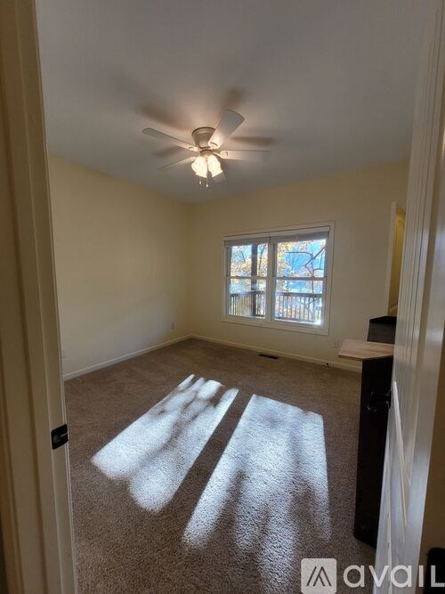 A room with a ceiling fan and a window letting in sunlight.