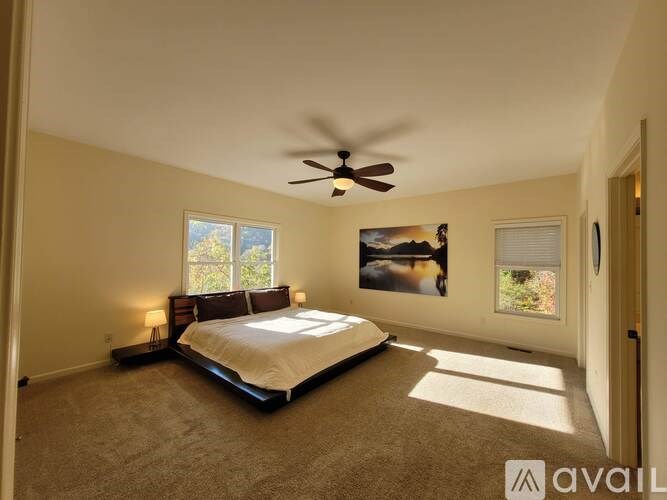 A bedroom with a bed, a ceiling fan, and a painting on the wall.