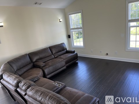 A living room with a brown leather couch and a window.