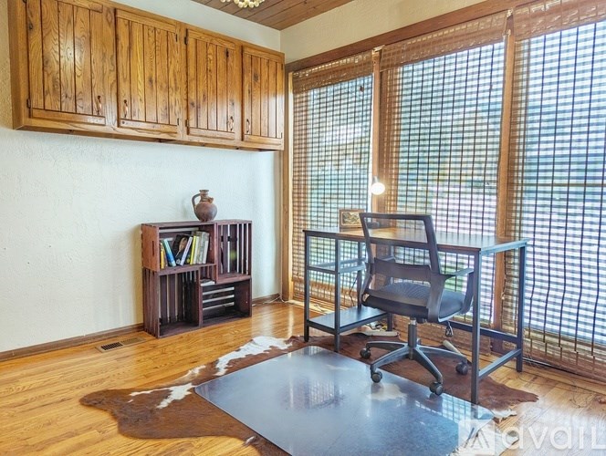 A room with a wooden floor, a black chair, and a cowhide rug.