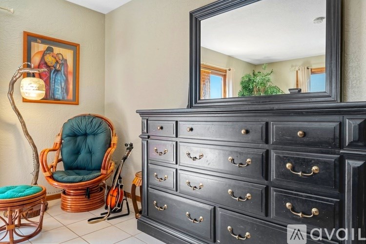A room with a black dresser, a chair, and a mirror.