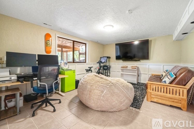 A room with a bean bag chair, a desk with a computer, and a TV on the wall.