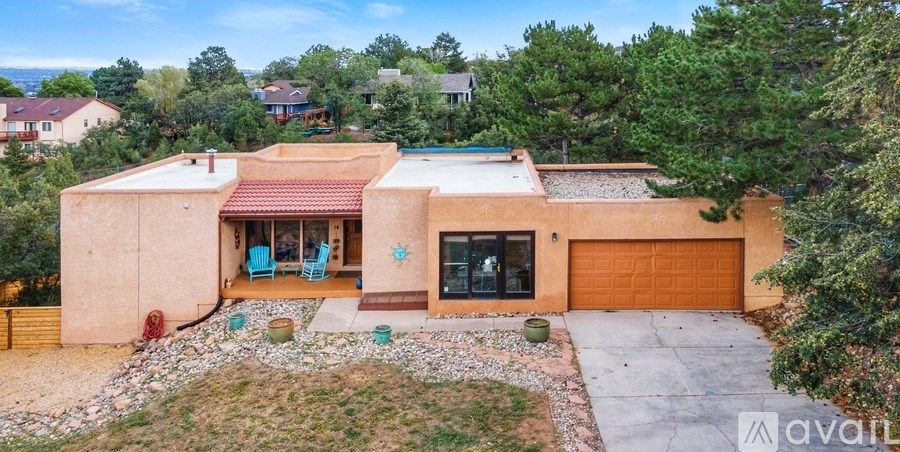 A house with a red roof and a brown garage door is surrounded by greenery.
