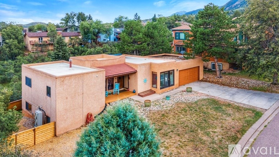 A house with a red roof is surrounded by greenery and other houses in the background.