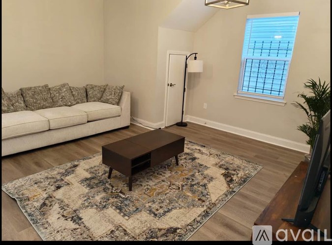A living room with a white couch, a rug, and a window with a view of a building.