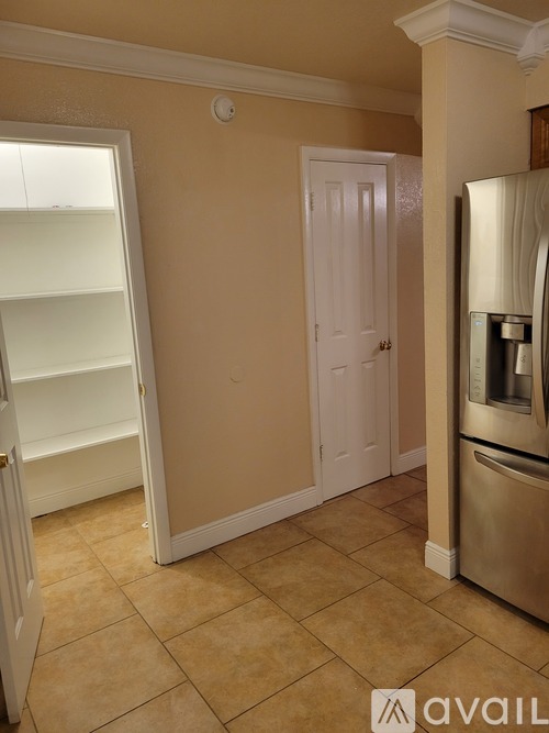 A kitchen with a refrigerator, a door open to a pantry, and a wall-mounted light fixture.