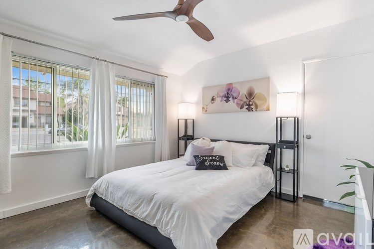 A bedroom with a large bed, a ceiling fan, and a window with white curtains.