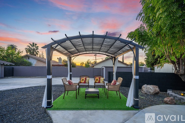 A patio with a canopy and chairs is set up in a backyard.