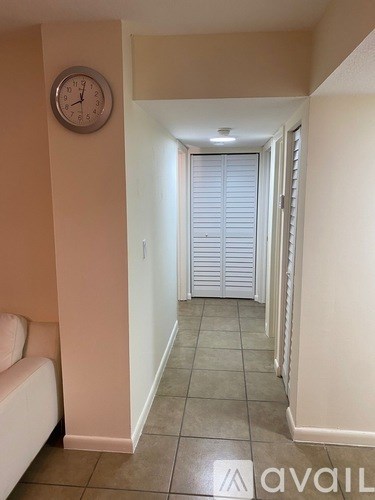 A hallway with a clock on the wall and a white couch on the left side.
