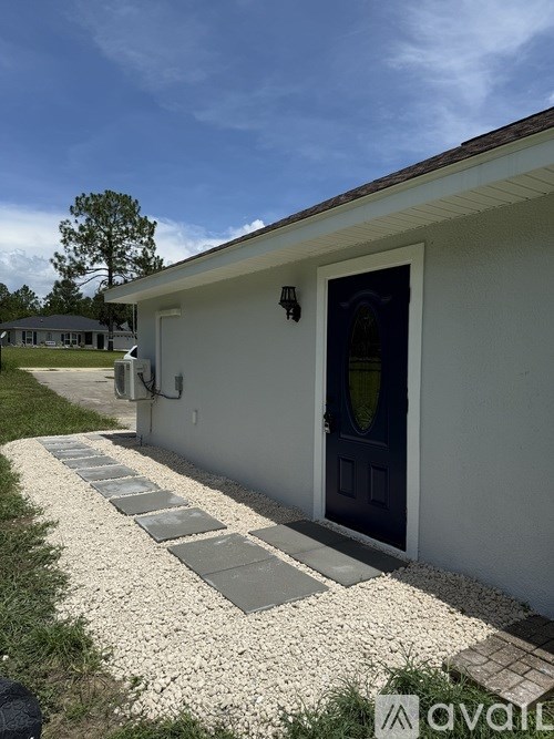 A white house with a black door and a gravel path leading to it.