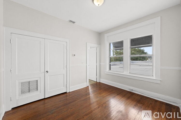 A room with white walls and wood flooring, featuring a window with a view of trees and a white door with a window above it.