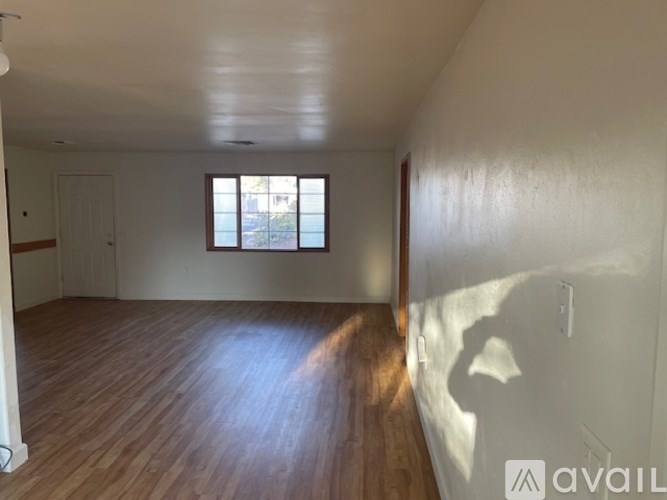 A room with wooden flooring and a window letting in sunlight.